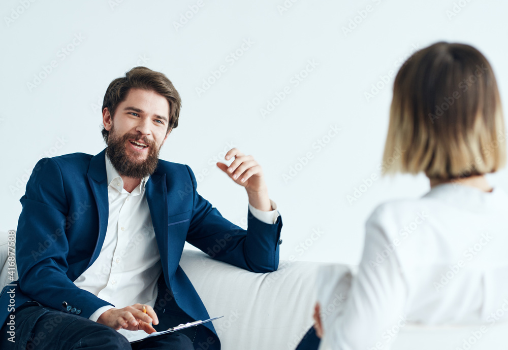 A man in a classic suit sits on the couch indoors with documents and a woman vacancies A man in a classic suit sits on the couch indoors with documents and a woman vacancies