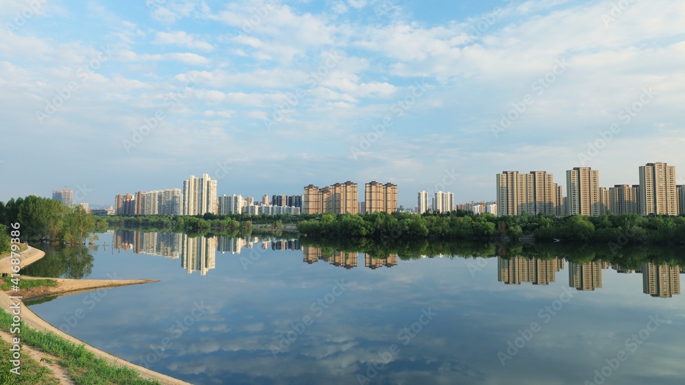 Reflection of city buildings and clouds on a calm park lake