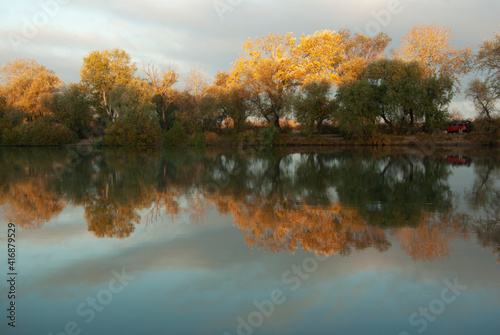 Autumn landscape with a river and trees reflected in the water.