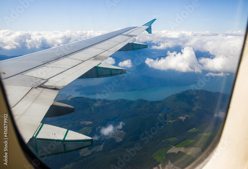 mountains, lakes and rivers outside a plane window. Travel time, sky, clouds and plane wing. Aerial view