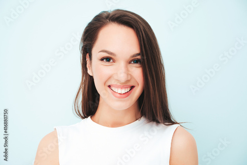Closeup portrait of young beautiful smiling female in trendy summer white t-shirt. Sexy carefree woman posing near light blue wall in studio. Positive model having fun indoors. Cheerful and happy