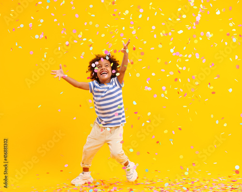 Excited African American kid jumping and catching confetti in studio