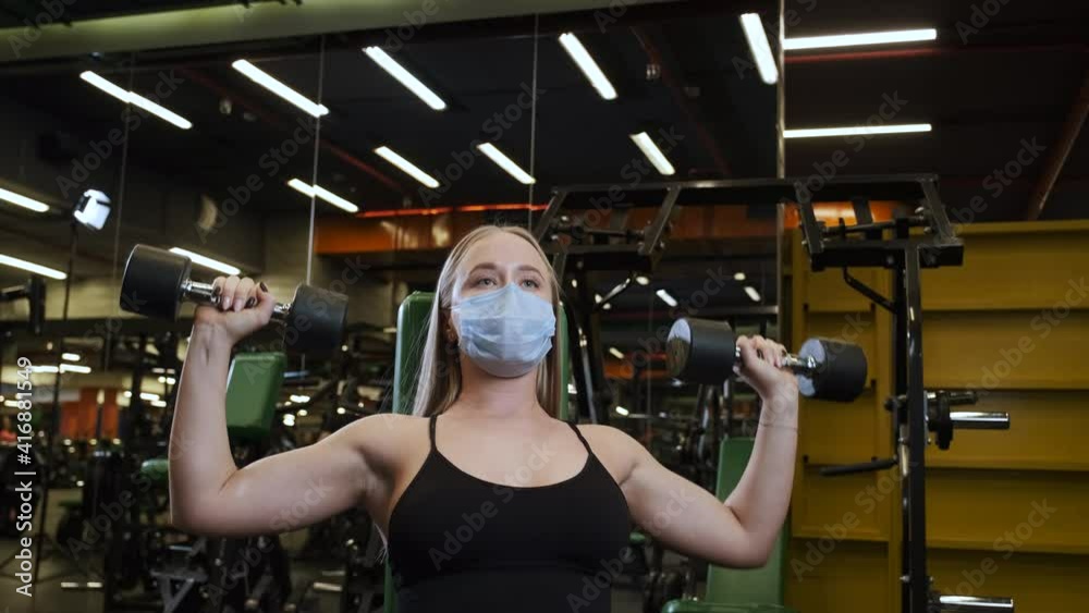 Woman doing exercises in gym using mask, following precautions due to COVID-19 Woman doing exercises in gym using mask, following precautions due to COVID-19