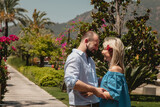 Loving couple enjoying honeymoon in luxury hotel, walking through grounds with palm trees and beauty flowers. Happy lovers on romantic trip have fun on summer vacation. Concept romance and relaxation