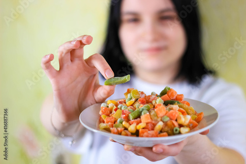 The girl is holding a plate of frozen vegetable mixture. The concept of diet and proper nutrition. Blurry.