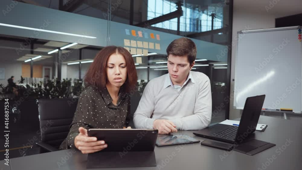 Man and woman working in office. Multiethnic business team doing research using tablet and laptop, Agile board on glass wall behind them. Concept of analysis Man and woman working in office. Multiethnic business team doing research using tablet and laptop, Agile board on glass wall behind them. Concept of analysis