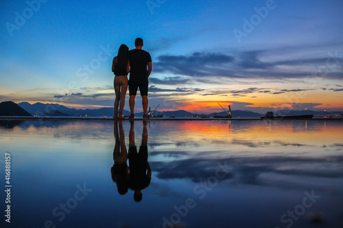 silhouette and reflection of romantic boy and girl friends holding hands and enjoying sunset at Water front at Western District Public Cargo Working Area, Kennedy town, Victoria Harbour, Hong Kong.