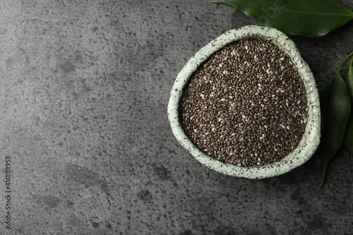 Bowl with chia seeds and leaves on grey table, flat lay. Space for text
