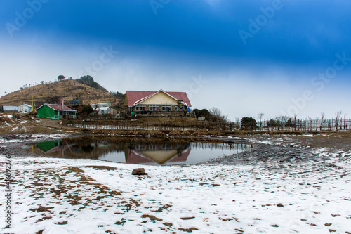 A trekkers hut in front of a small pond at Tunglu near Darjeeling with lots of snow and cloudy sky. photo