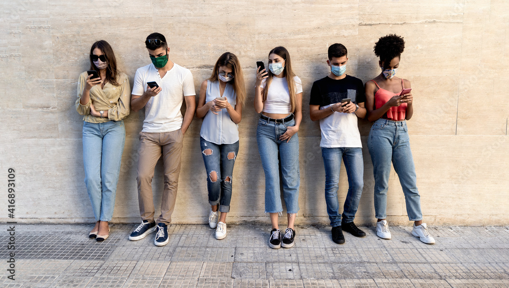 group of multiracial friends with face masks in front of a clean wall using smartphones to sharing content on social networks. Covid-19 and technology lifestyle  concept - obrazy, fototapety, plakaty 