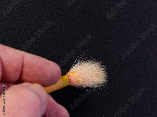 Close-up of the tips of the finger holding a paint brush with a bamboo grip on black background