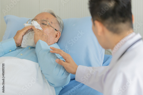 An old fat asian male patient with gray hair wearing eyeglasses and light blue shirt have runny nose and try to blow the snot out to the white clean tissue when doctor wearing whit lab coat 