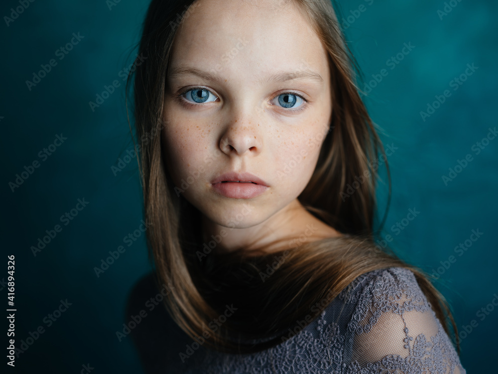Portrait of a beautiful little girl in a gray dress on a turquoise background and blue eyes