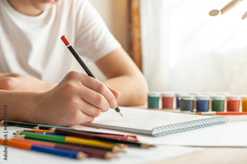 A teenage child draws. The hand of a teenage boy with a pencil. Creative hobby. Drawing lesson. Close-up and selective focus. A teenage child draws. The hand of a teenage boy with a pencil. Creative hobby. Drawing lesson. Close-up and selective focus.