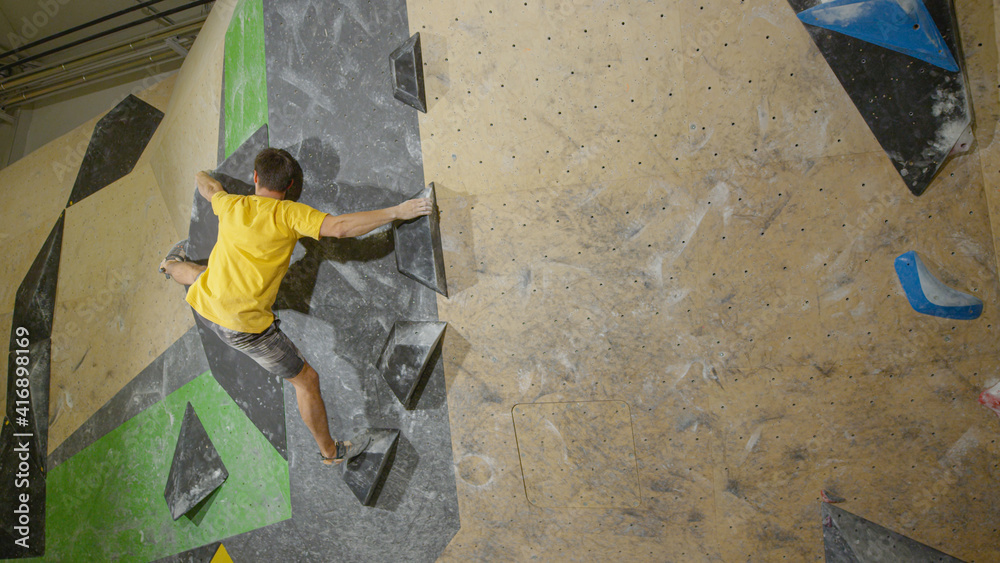 COPY SPACE: Athletic young man holds on to black volume holds while bouldering. COPY SPACE: Athletic young man holds on to black volume holds while bouldering.
