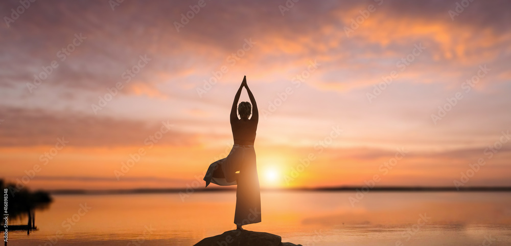Young woman doing yoga exercise in stunning sea and sunset.