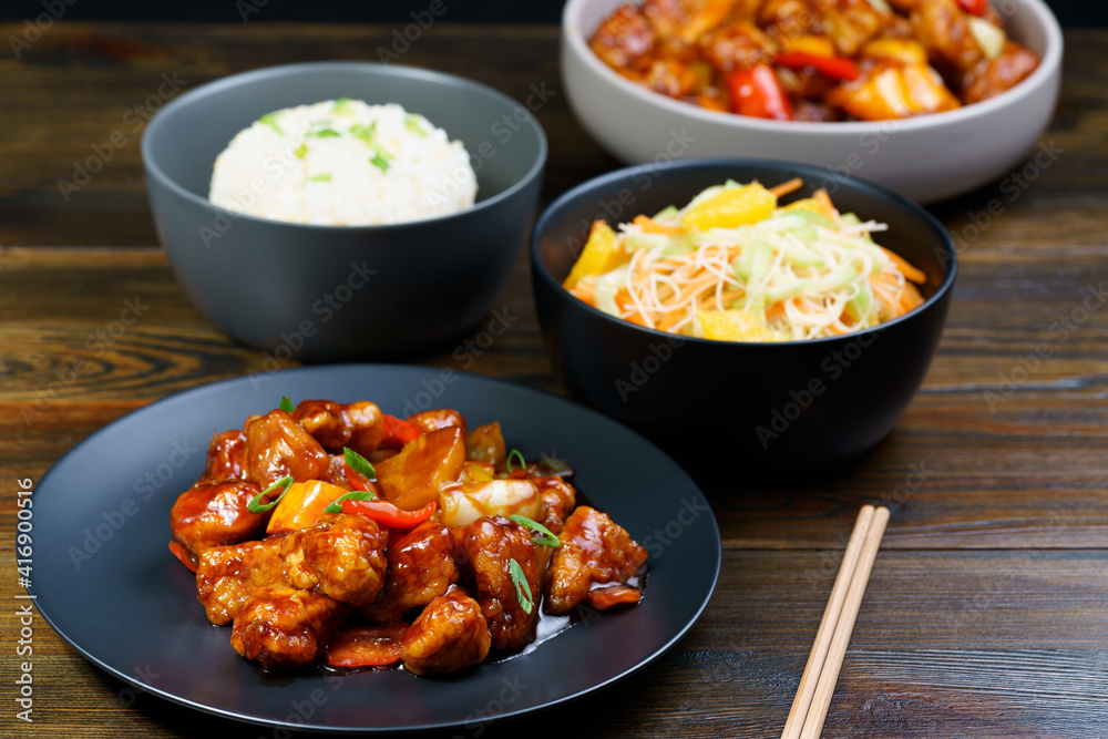 Sweet and sour chicken, fried rice with egg and glass noodles salad served in ceramic bowls. Dark wooden table, high resolution Sweet and sour chicken, fried rice with egg and glass noodles salad served in ceramic bowls. Dark wooden table, high resolution