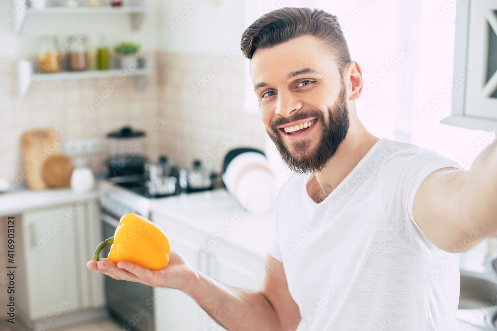 Young handsome happy bearded man with smart phone in the kitchen at home while he is preparing the healthy fresh vegan salad and making selfie photo Young handsome happy bearded man with smart phone in the kitchen at home while he is preparing the healthy fresh vegan salad and making selfie photo