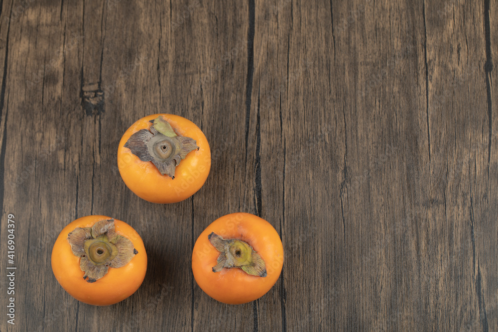 Three ripe persimmon fruits placed on wooden surface