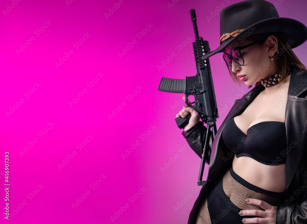 a stylish woman in black clothes and a hat poses on a neon background with an airsoft gun