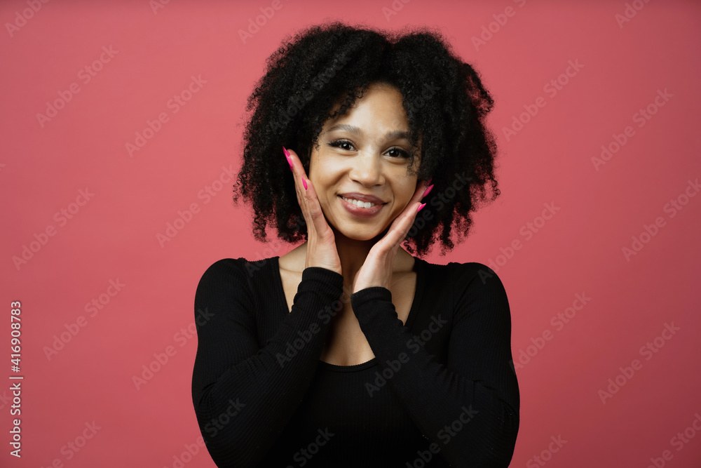 smiling emotion hands near the face of a young beautiful woman Afro appearance ethnic. Looks at the camera and smiles, curly brunette black hair. the background color fuchsia