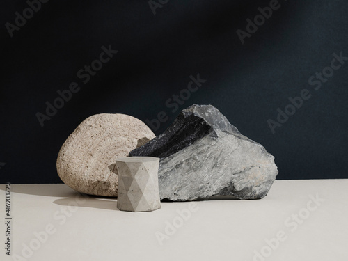 Minimal modern colorful beauty background for branding and product presentation. Still life mock up photo of a stones and a concrete form with long shadow on beige table and dark wall.