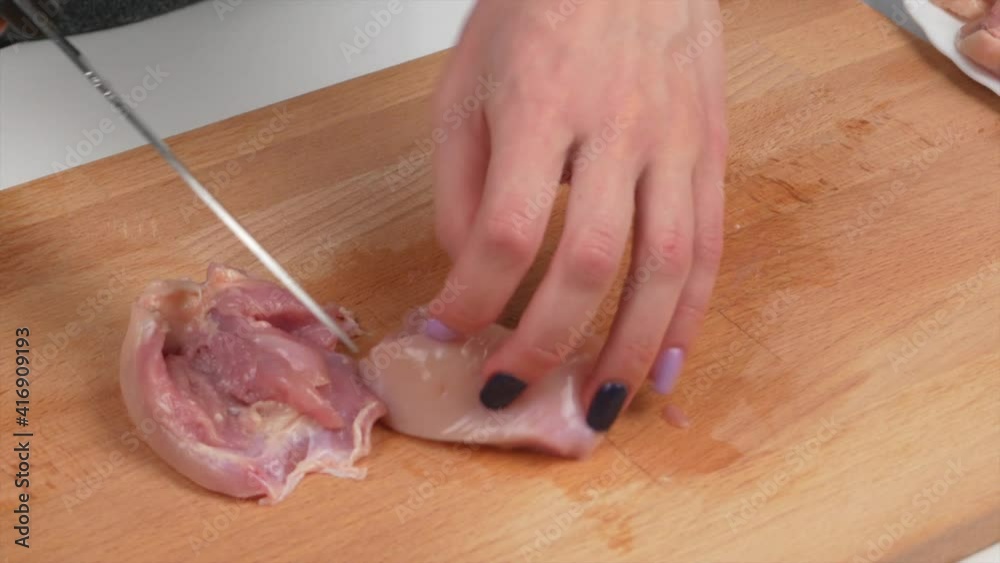 Woman cuts chicken on wooden kitchen cutting board for making curry, close-up Woman cuts chicken on wooden kitchen cutting board for making curry, close-up
