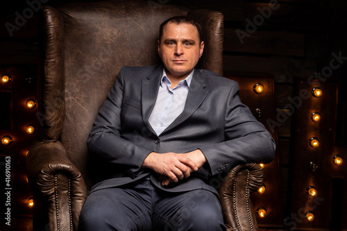 handsome businessman in a suit looks at the camera on a leather chair.