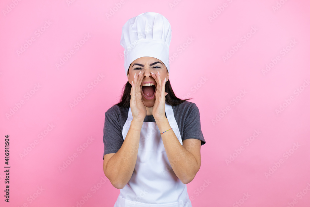 Young hispanic woman wearing baker uniform over pink background shouting and screaming loud to side with hands on mouth Young hispanic woman wearing baker uniform over pink background shouting and screaming loud to side with hands on mouth