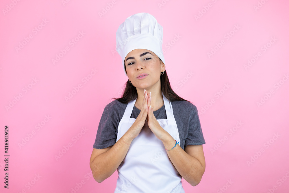 Young hispanic woman wearing baker uniform over pink background with Hands together and fingers crossed smiling relaxed and cheerful. Success and optimistic Young hispanic woman wearing baker uniform over pink background with Hands together and fingers crossed smiling relaxed and cheerful. Success and optimistic