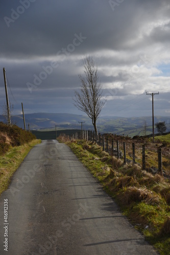 a small road that leads to llyn marw near caersws in wales, surrounded by fields and barbed fences photo