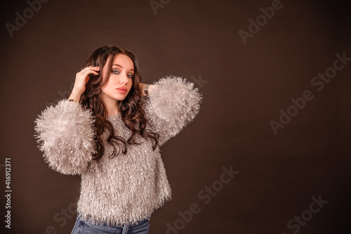 beautiful girl poses on a black gray background. lady in jeans and grey fluffy sweater