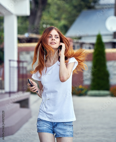 cheerful woman in a white t-shirt walks down the street in headphones with a phone rest © SHOTPRIME STUDIO