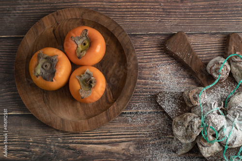 Plate of fresh fuyu and dried persimmon fruits on wooden board
