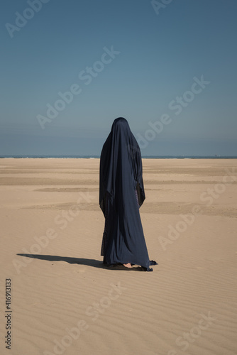 conceptual fineart portrait of a woman on the beach near the ocean covered by blue fabric photo