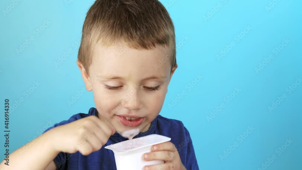 Little boy eatiing yogurt on blue background Little boy eatiing yogurt on blue background