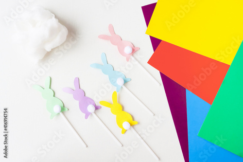 Colorful paper rabbit figures with fluffy cotton wool tails. DIY concept, preparation of decor.