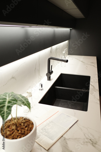 Modern kitchen with black furniture  White marble worktop and backsplash. Black sink and tap  Light under wall cabinet.