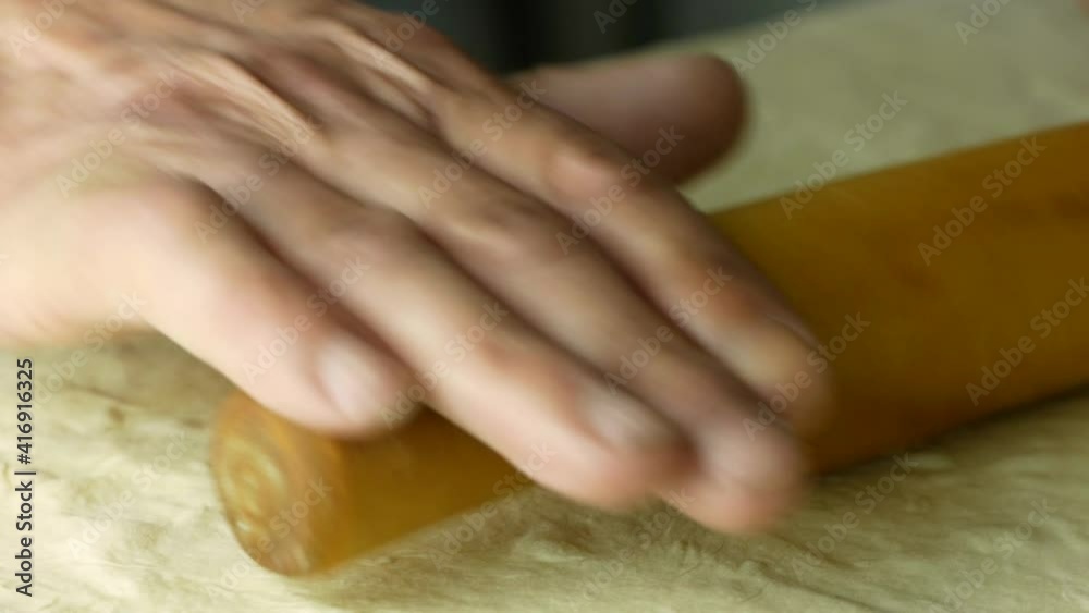 Homemade bread baked by senior citizen theme. Close-up of an elderly man's hand rolling out the dough with a rolling pin. Making homemade pie. Selective focus, shallow depth of field