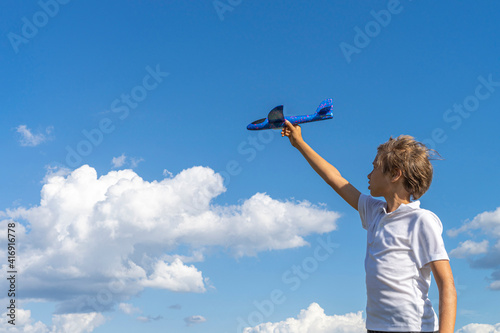 Boy playing with blue toy plane against blue sky at sunny day outdoors