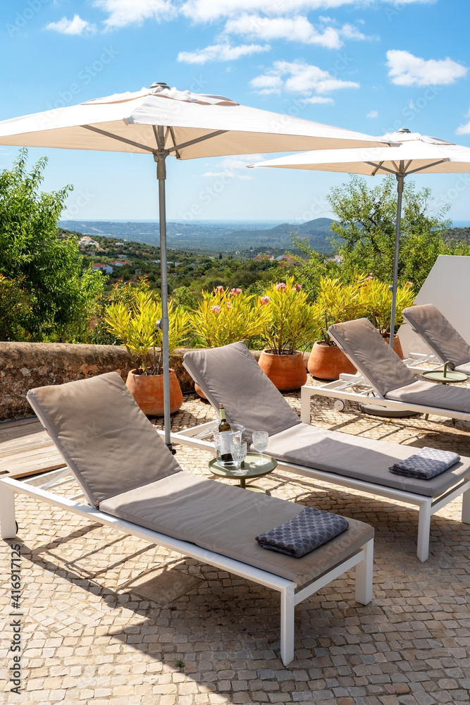  Loungers with umbrellas to provide shade, a bottle of wine on a small table, and a nice aesthetic mountainous view on a clear sunny day.