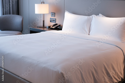 Clean Bedding sheets and pillow on natural wall room background. White bedding and pillow in hotel room. White pillows on empty bed.