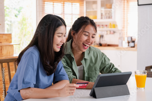 Asian lesbain couple using tablet and credit card to shopping online on kitchen table in home.couple lgbtq lifestyle concept