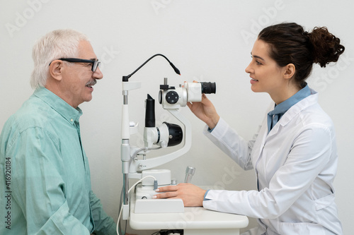 Ophthalmologist using medical equipment while testing eyesight of male patient