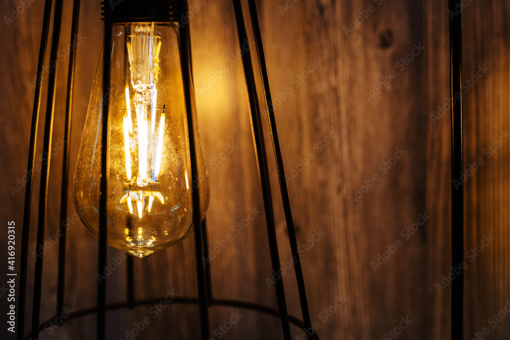 Modern retro style lamp in a shade made of metal rods against a background of a wooden wall. Copy space