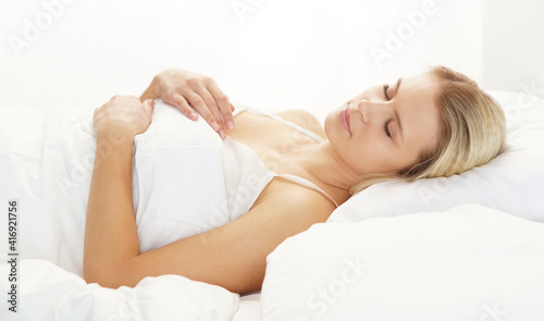 Young and beautiful blond girl in the bed. Sleeping woman in a rays of morning sun.