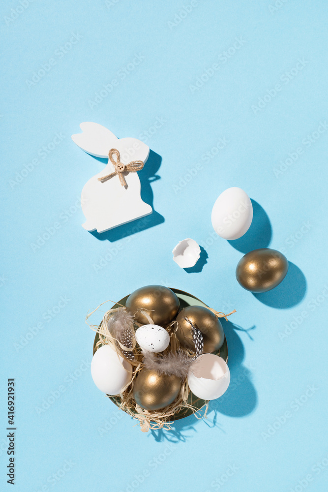 Easter white golden eggs, quail eggs and feathers on blue background.