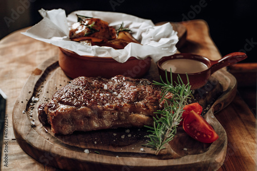 Juicy delicious steak with sauce baked potatoes on a wooden surface