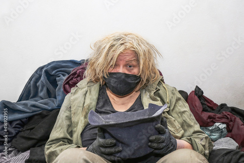 a homeless woman in a mask and gloves with a hat in her hands