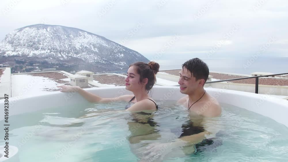 couple relax in the hot pool in the winter outdoors with sea and mountain views couple relax in the hot pool in the winter outdoors with sea and mountain views